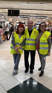 tre persone sorridono alla macchina fotografica. sullo sfondo le corsi di un supermercato